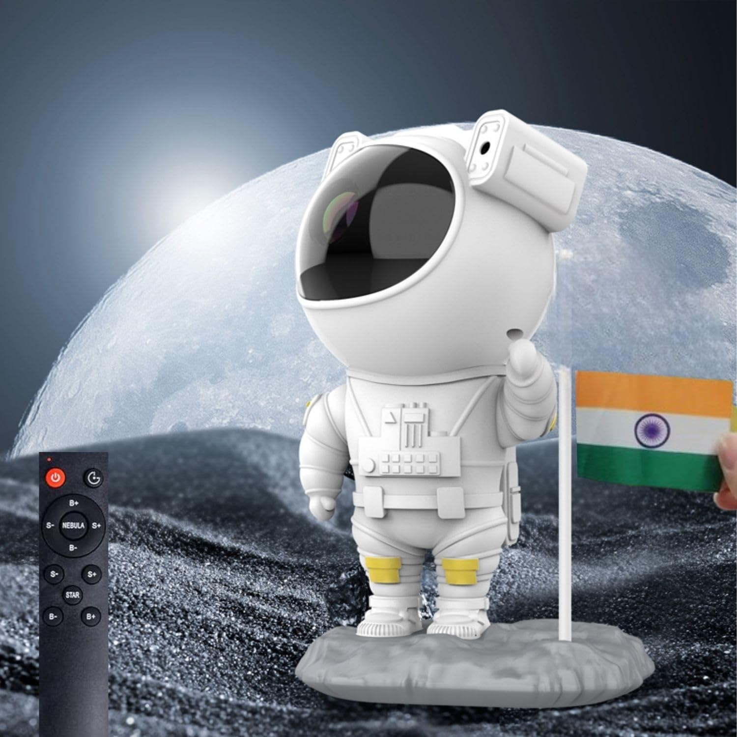 A toy astronaut holding an Indian flag stands on a rocky surface, evoking a lunar landscape. A remote control lies on the left, suggesting the use of a space projector. The bright, full moon in the background enhances this Astronaut Galaxy Projector-themed scene.