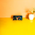 A wallet and a purse on a bright yellow table beside a cheerful vase of flowers.